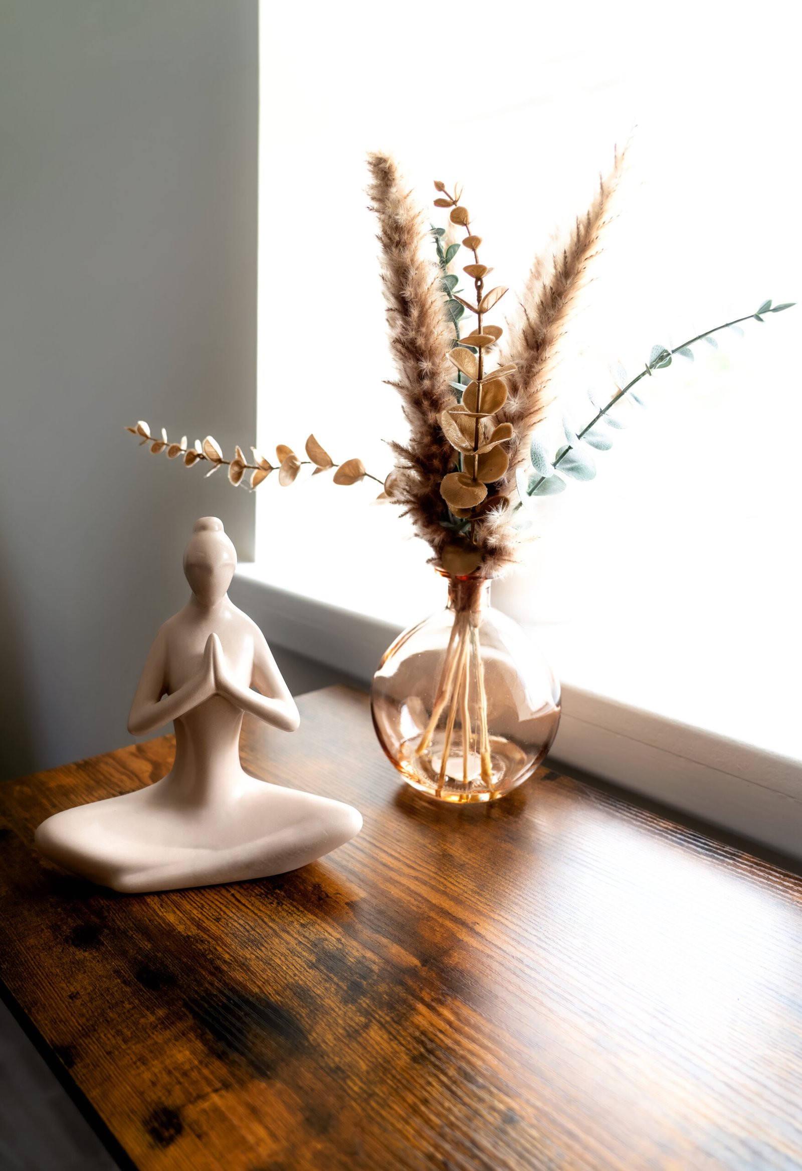 Serene yoga figurine and vase with dried flowers on a wooden table, symbolizing peace and mindfulness.
